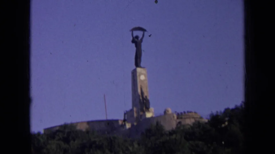 Final 1963 Russia 8mm frame of the distant hilltop statue, with pedestal, trees, sky, and visible film specks.