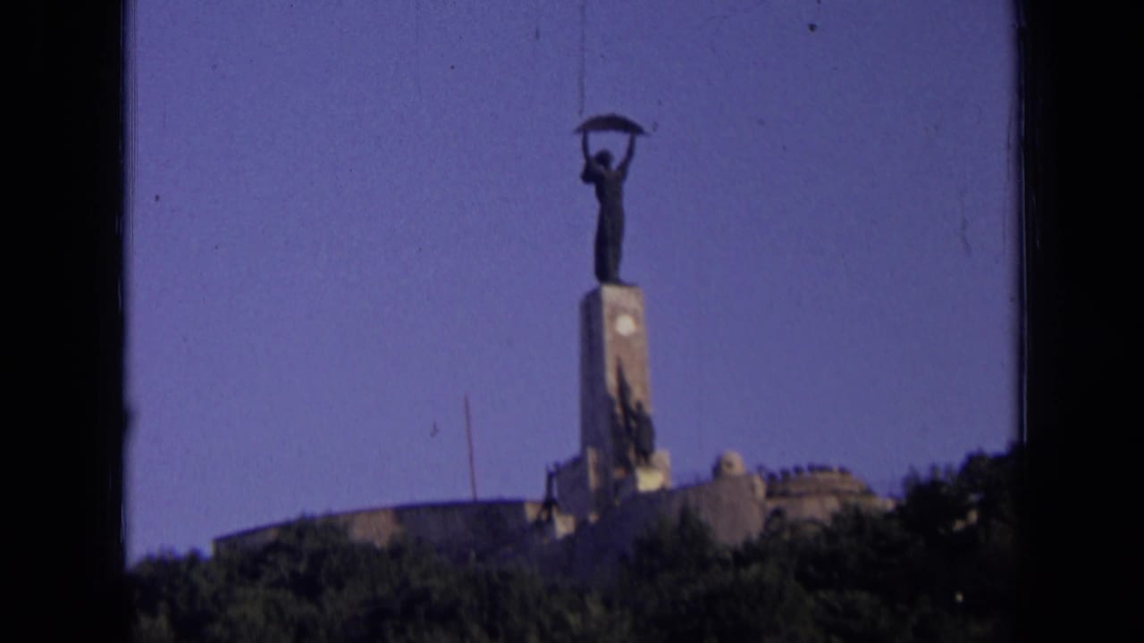 Distant statue on a hilltop monument framed by trees and blue sky.