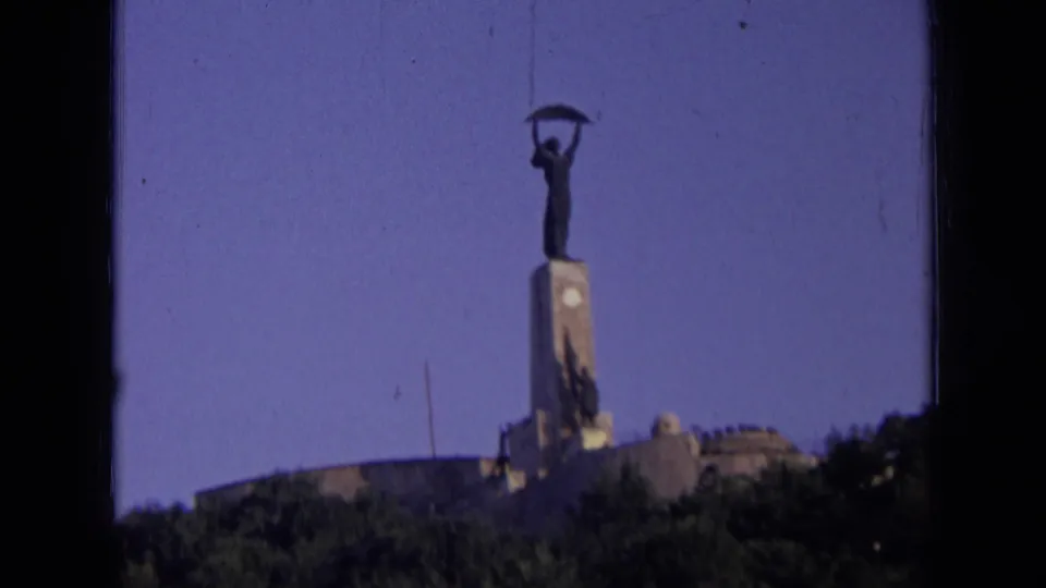 Low-angle 1963 Russia home-movie frame of a hilltop Soviet-era monument with a metal figure above a stone base.