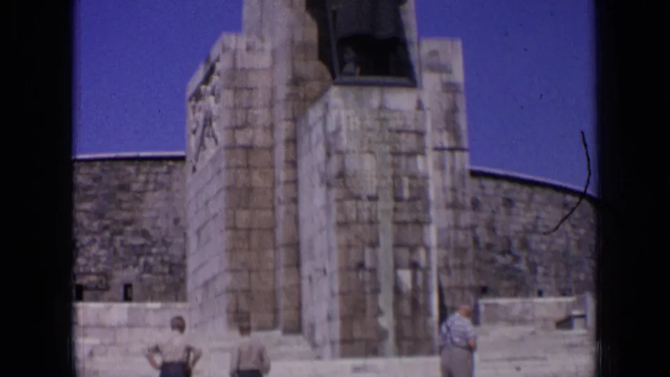 1963 Russia home-movie frame showing the monument base, curved wall, and adult visitors providing scale.