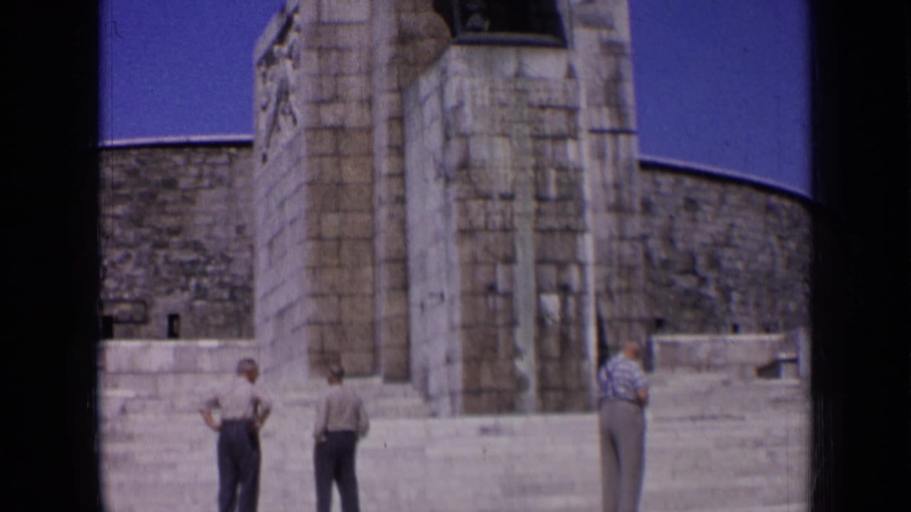 1963 Russia home-movie frame showing three men in casual clothing near broad steps and a monumental stone facade.