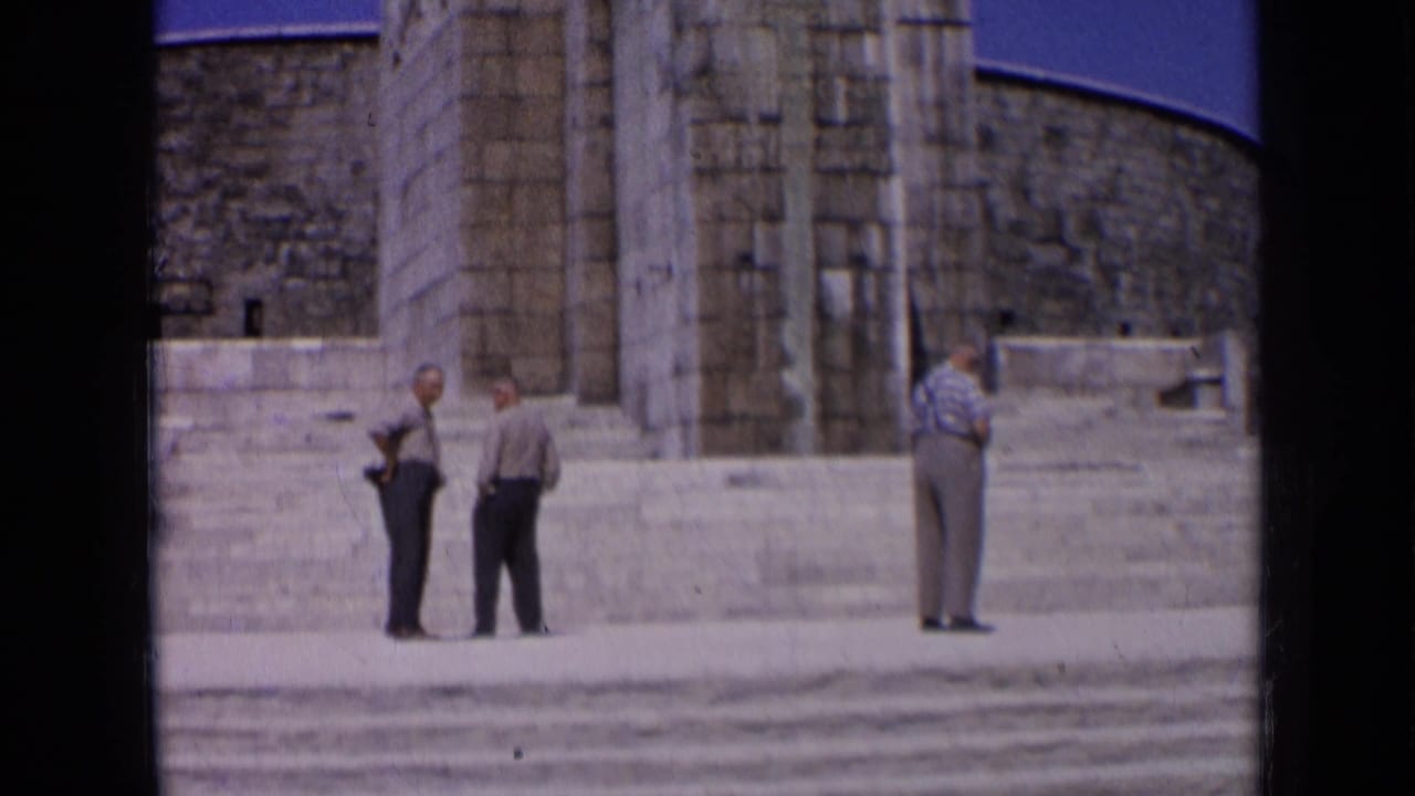 1963 Russia frame with two men conversing and another standing apart near a monumental stone entrance and steps.