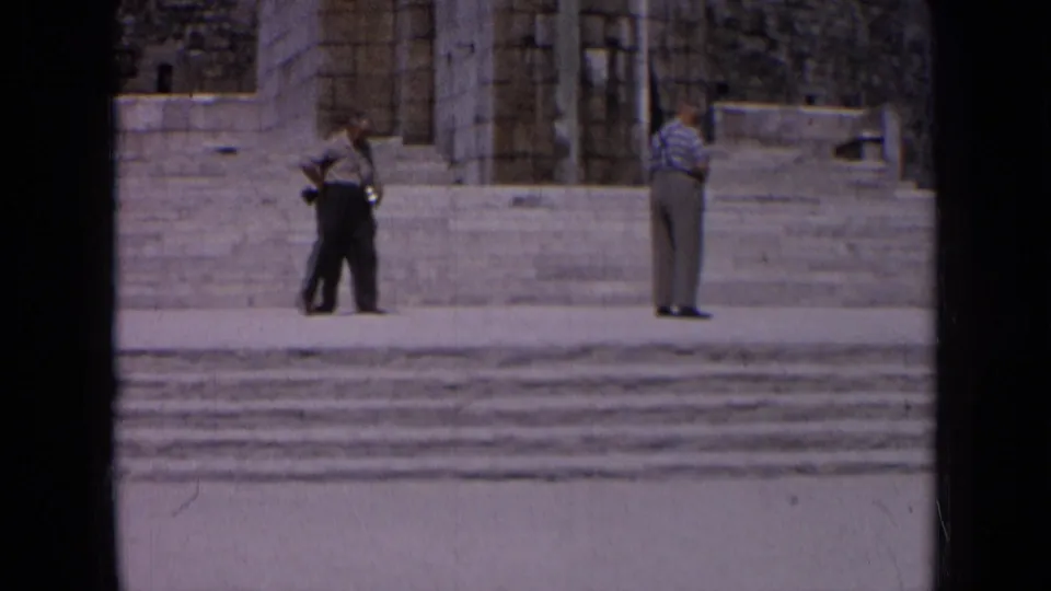 1963 Russia home-movie frame showing men moving and standing near a stone stairway and monumental facade.
