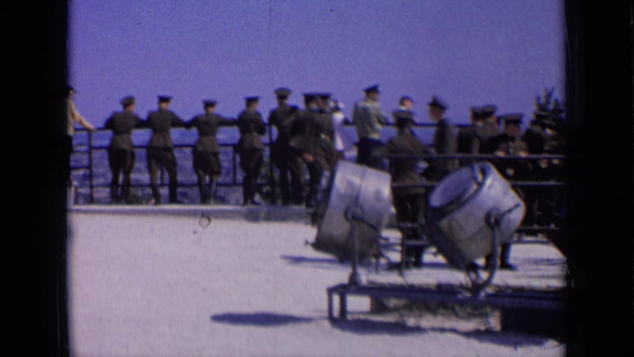 Uniformed men cluster near a railing as searchlights sit on a foreground platform.