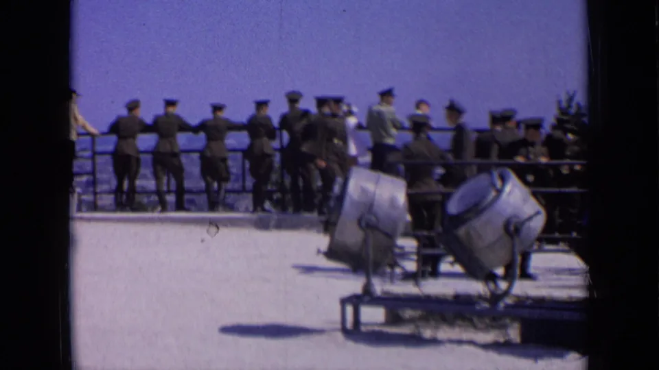 Uniformed men and civilians appear at an elevated railing in Russia, with large mounted searchlights in front.