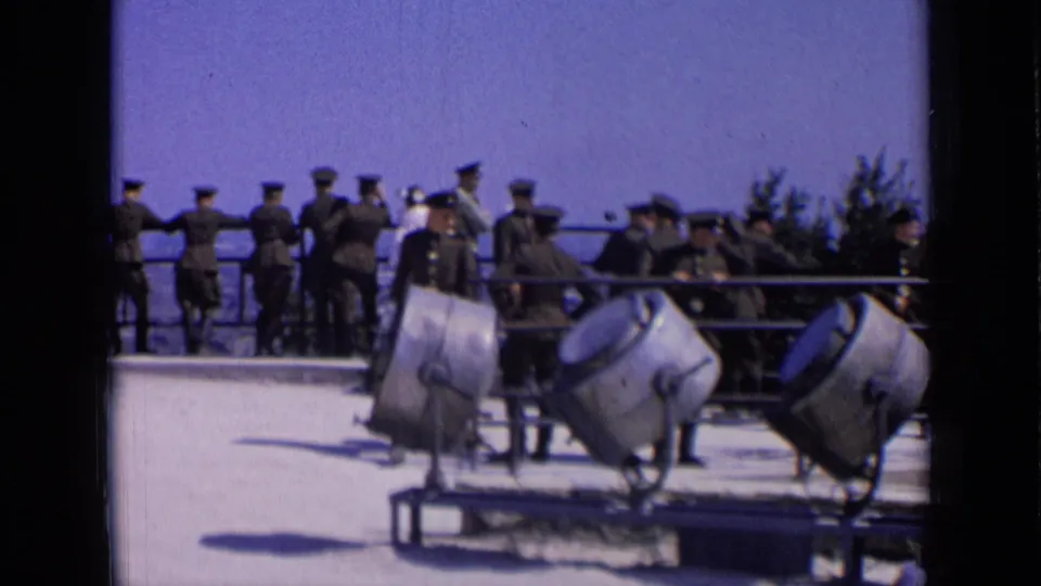 1963 Russia home-movie frame with uniformed men, civilians, and three large angled searchlights at an overlook.