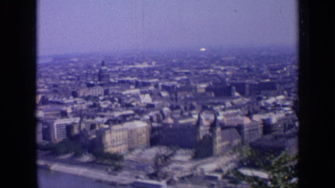 Elevated city panorama with riverbank buildings, haze, and dark vertical frame borders.