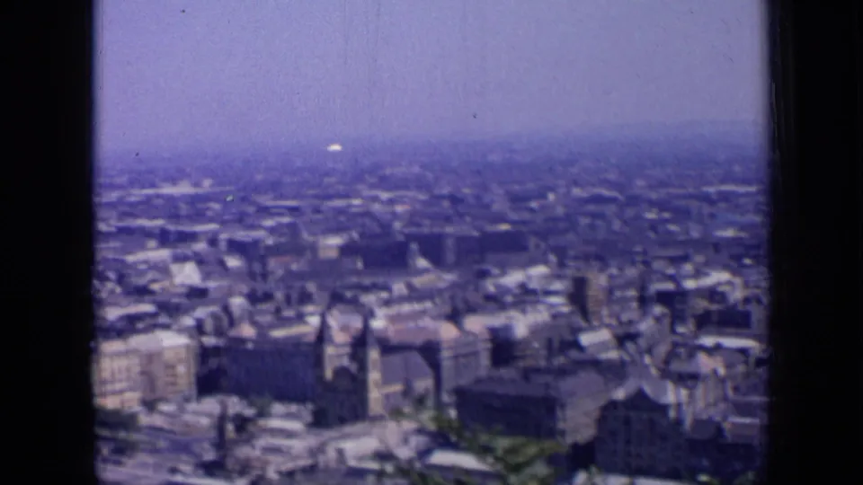 1963 Russian 8mm frame with rooftops, river edge, and a tower-like structure in a soft, purple-tinted city panorama.