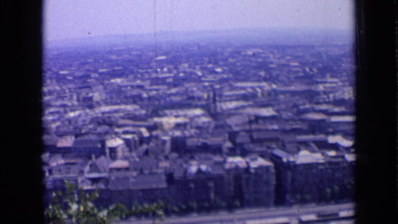 Hazy city view seen through dark 8mm frame borders with rooftops and trees below.