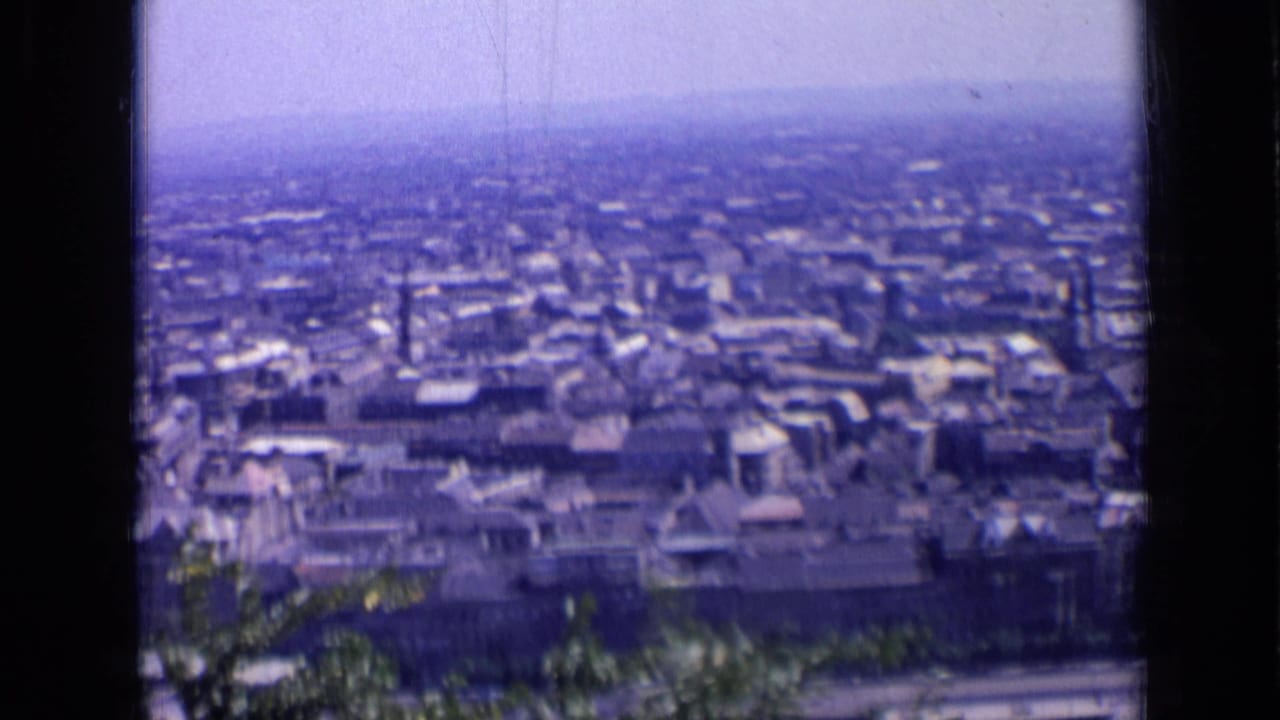 Soft blue-tinted city panorama with rooftops, haze, and dark vertical frame edges.