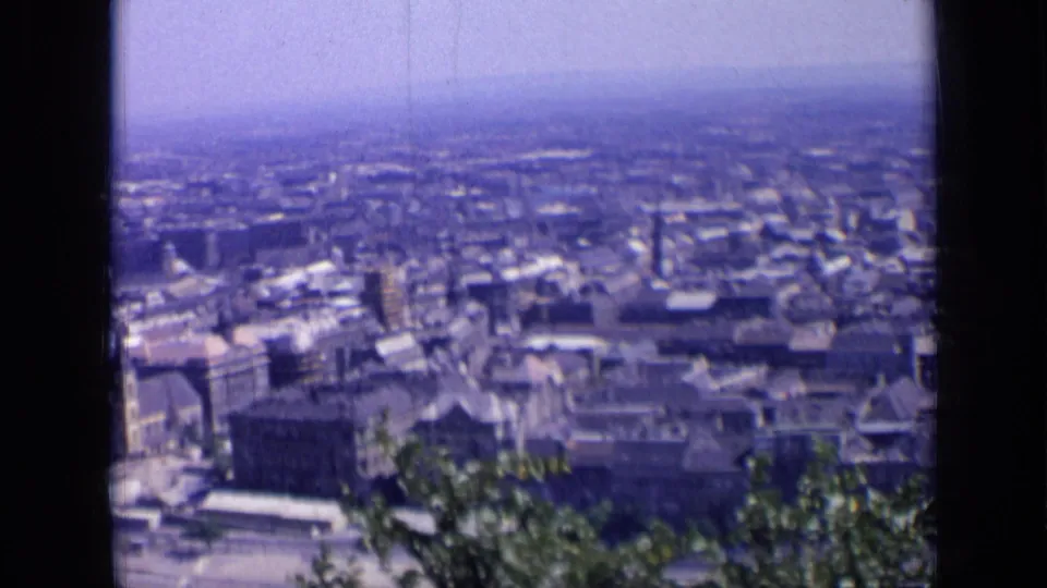1963 Russia home-movie view over city rooftops, with foreground greenery moving below a hazy blue sky.
