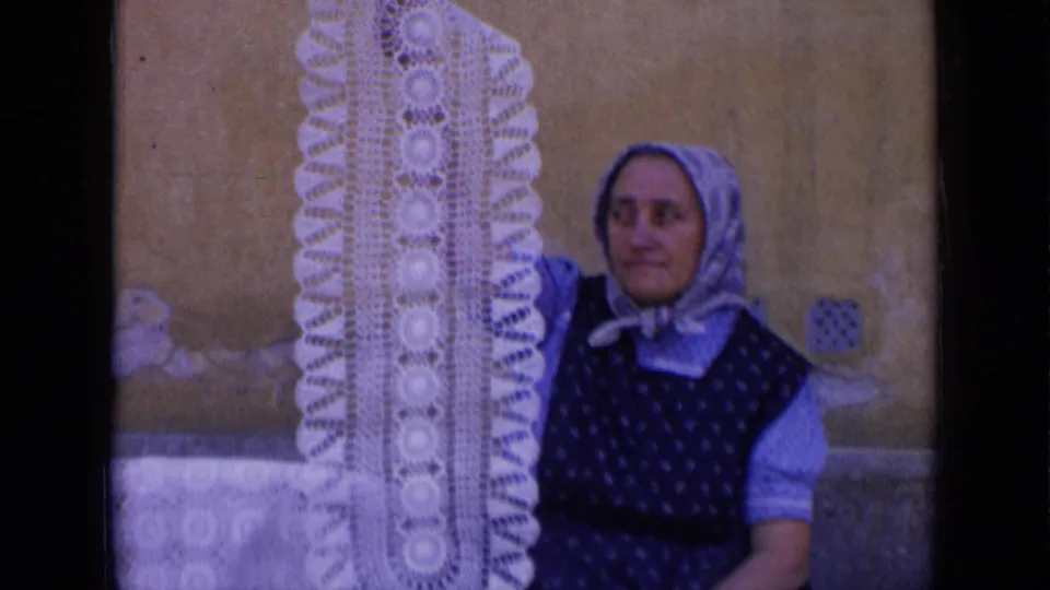 The 8mm frame shows a headscarfed woman near a long white crocheted doily, with soft focus and faded color.