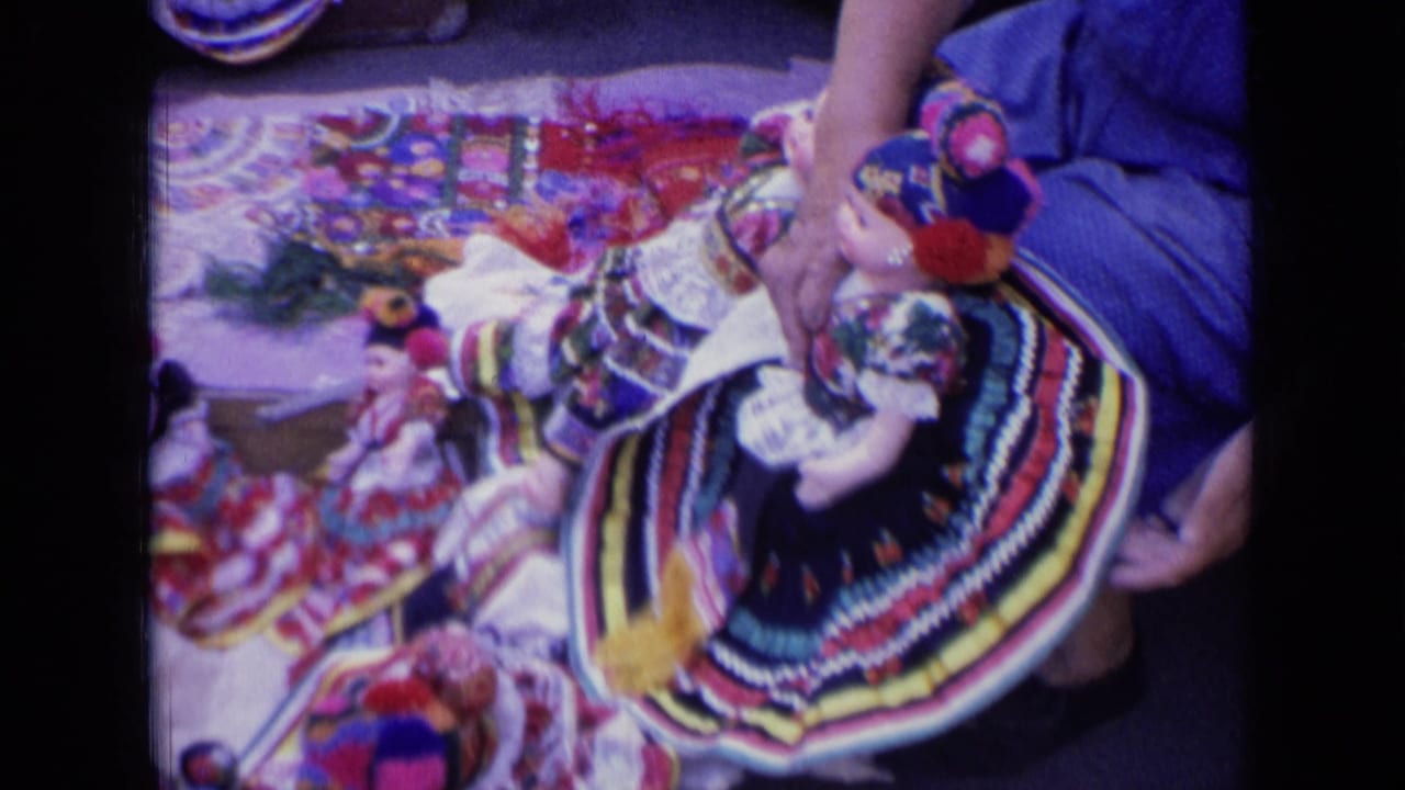 Hands arranging colorful rag dolls on a patterned cloth.