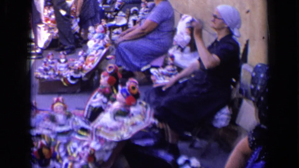 Two women sit beside a spread of colorful traditional-style rag dolls in 1963 Russia home-movie footage.