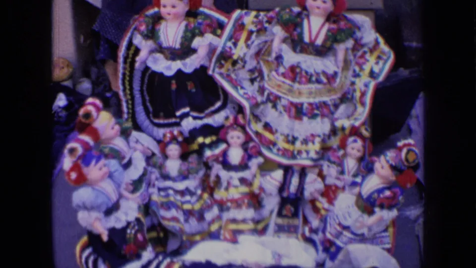 1963 Russia home-movie frame with multiple folk-costume dolls arranged closely, including layered skirts and head coverings.