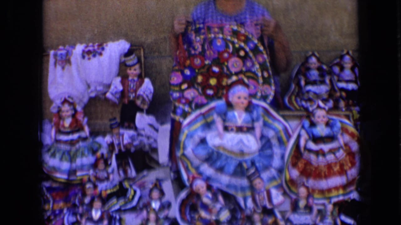 Woman displays colorful handmade dolls and textiles on a table.