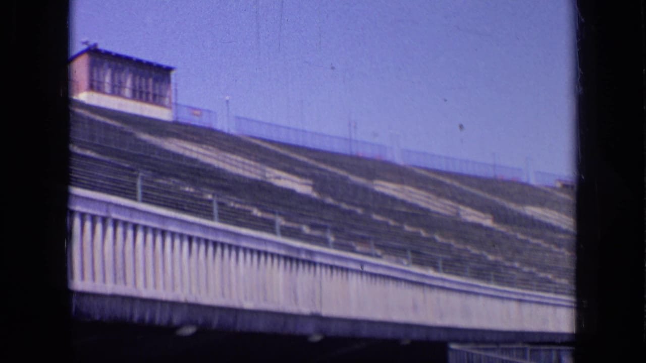 Empty stadium seating with railings and an upper structure under blue sky.