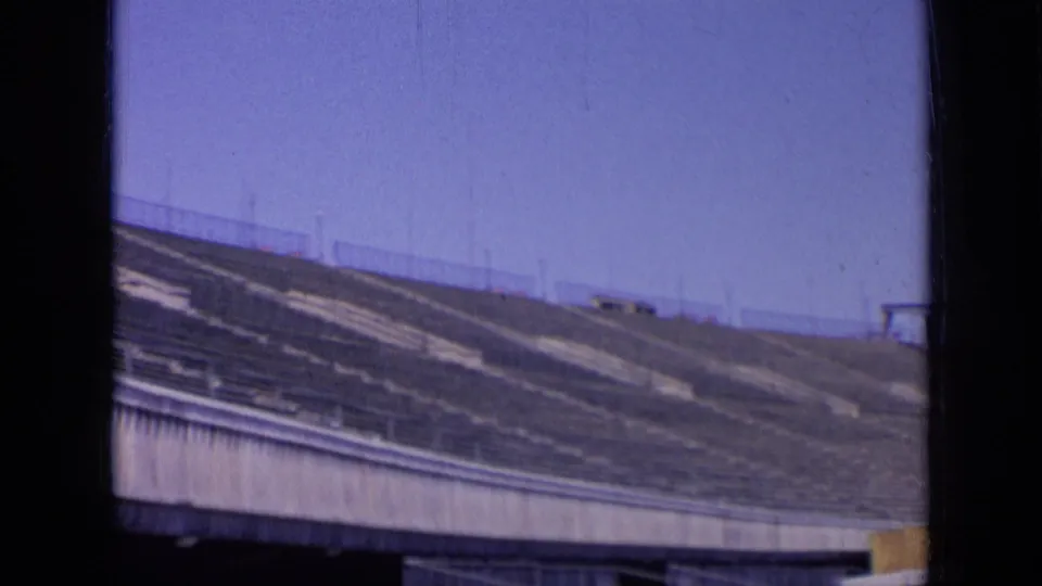 Angled 1963 8mm view of empty stadium seating, concrete tiers, and railings in Russia beneath clear blue sky.