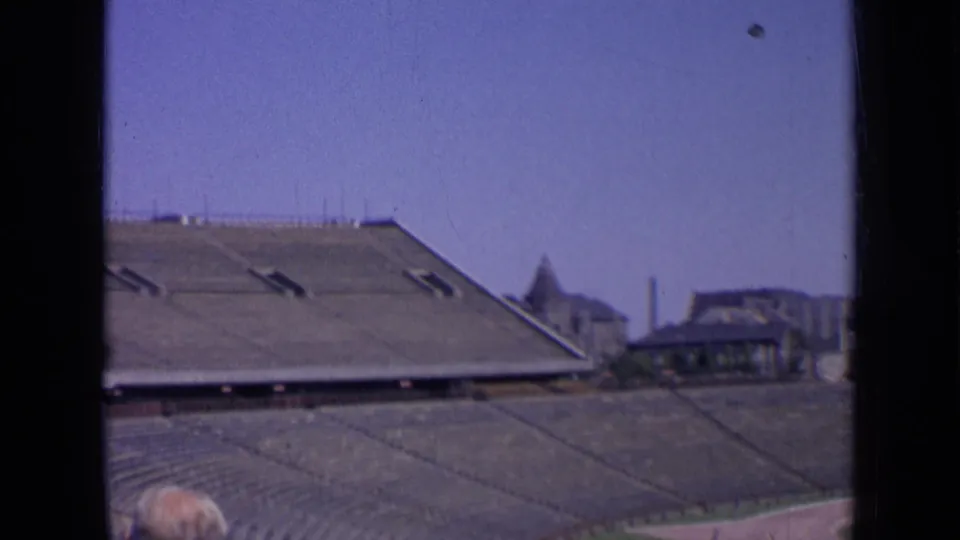 1963 Russia 8mm frame showing empty stadium bleachers, distant buildings, and a partially visible spectator head.