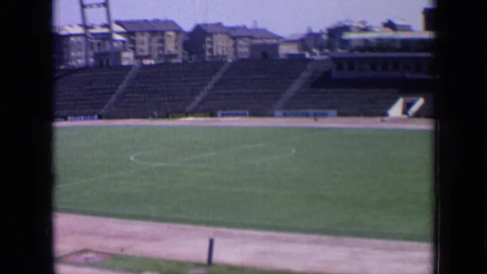 Final 8mm frame across the 1963 Russian stadium, with field, track, empty seating, buildings, and a tower in view.