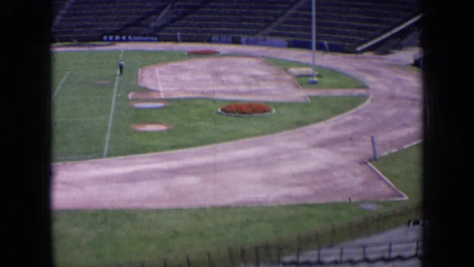1963 Russia home-movie frame showing an empty sports ground with paved perimeter, field edge, pole, and concrete seating.