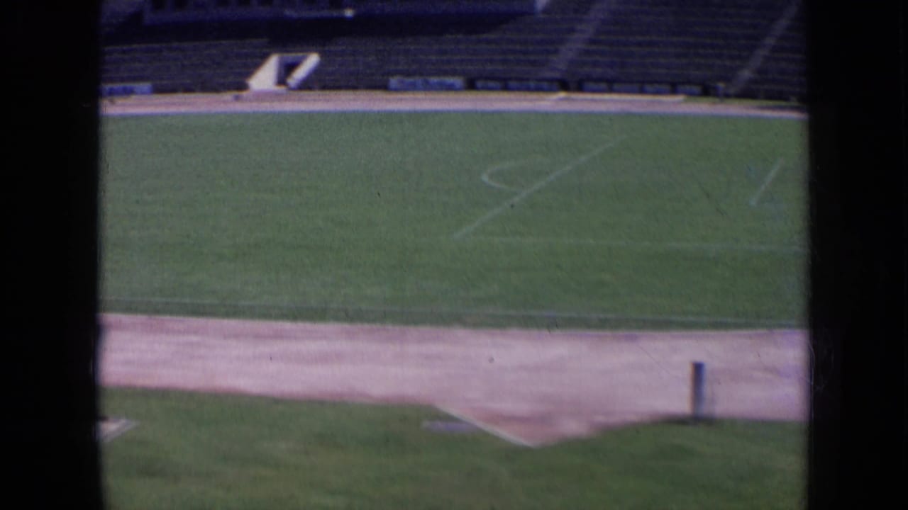 Wide stadium field seen through dark vertical window bars, with empty stands in the background.
