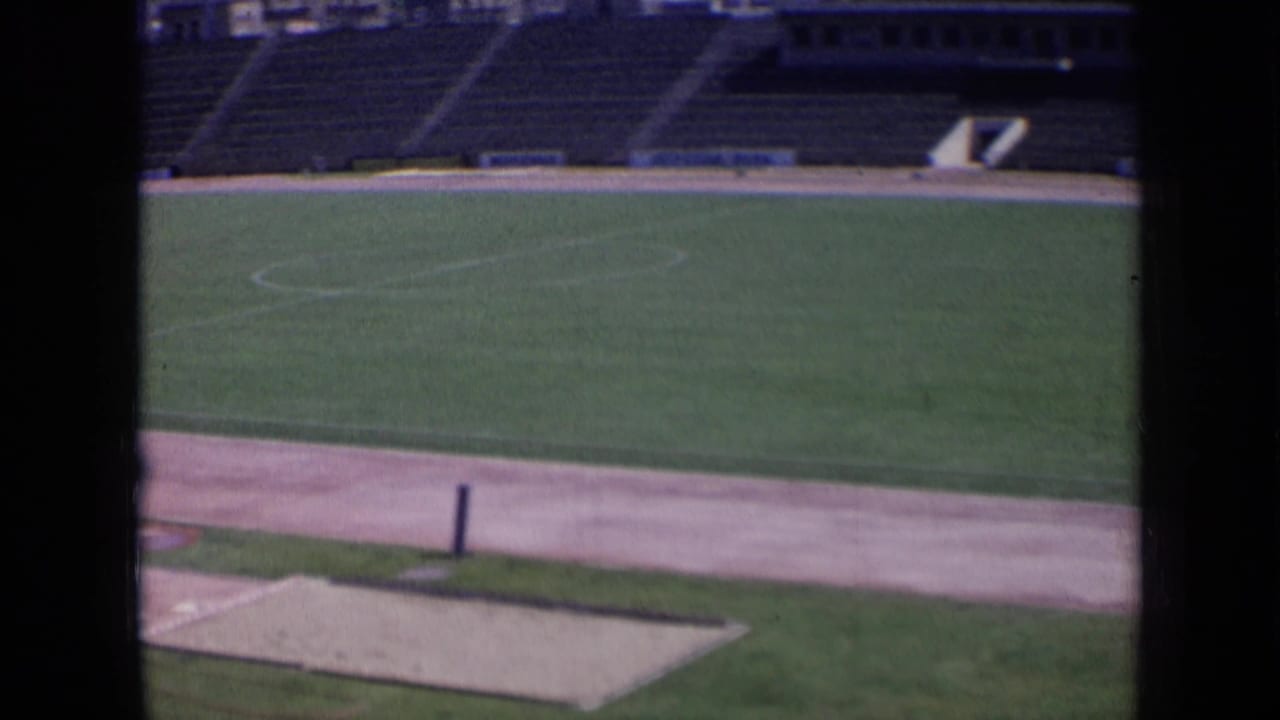 Stadium field and track viewed through dark bars, with empty stands and a tunnel opening beyond.
