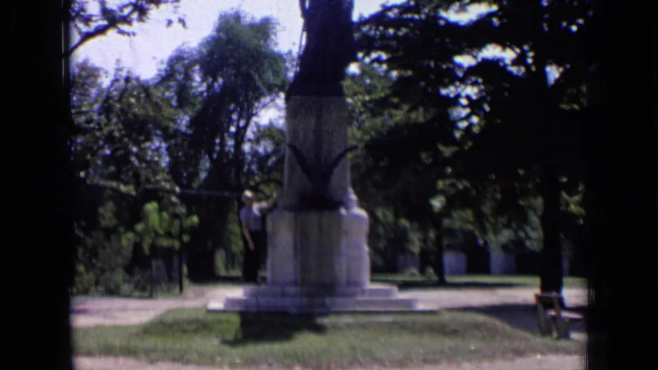 1963 Russia home-movie frame showing a person in a light shirt and dark trousers beside the Dzerzhinsky monument in a tree-lined park.