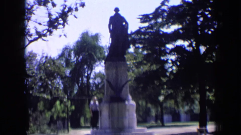 1963 Russia frame showing the Dzerzhinsky monument from a shaded vantage point, with a person at the base and trees across the background.