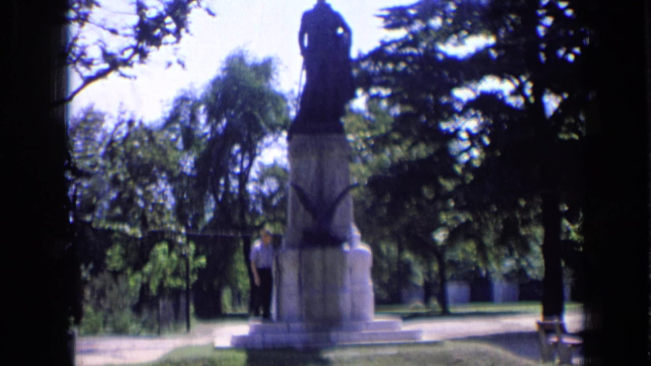 1963 Russia 8mm frame showing a man near a tall stone memorial in a green park under bright sky.