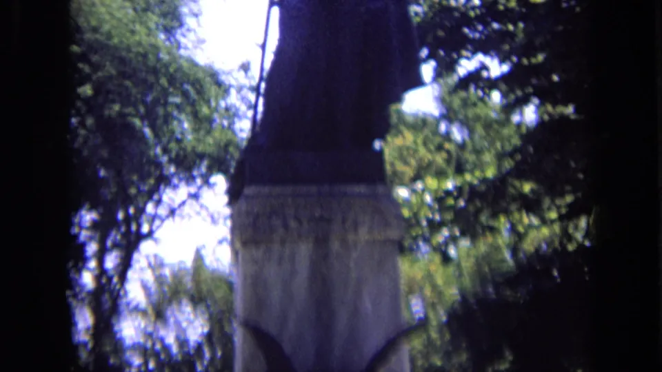 Tall stone statue on a memorial base appears among trees in 1963 Russia home-movie footage.
