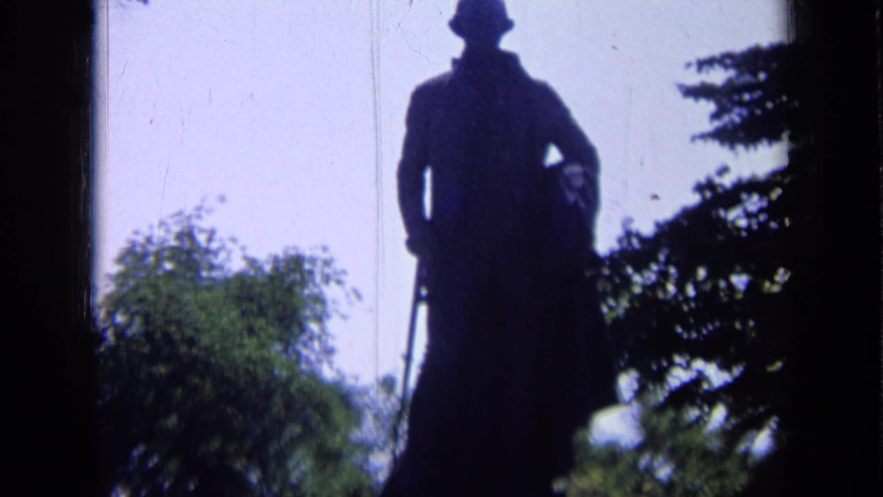 1963 Russia 8mm frame of a backlit standing statue in a hat, with trees and pale sky in the background.