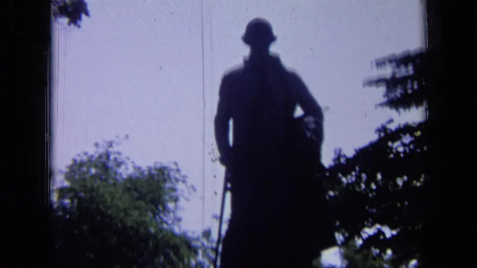 1963 Russia 8mm frame with the silhouetted statue centered below pale sky and leafy park vegetation.