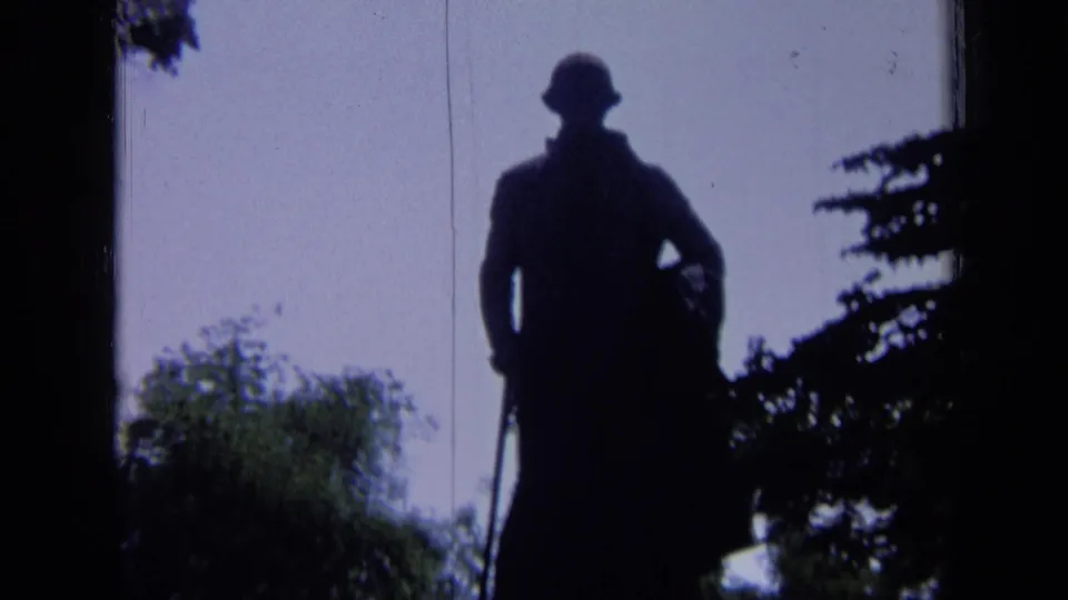 1963 Russia 8mm frame showing the dark outdoor statue with hat and cane-like detail, bordered by trees and film edges.