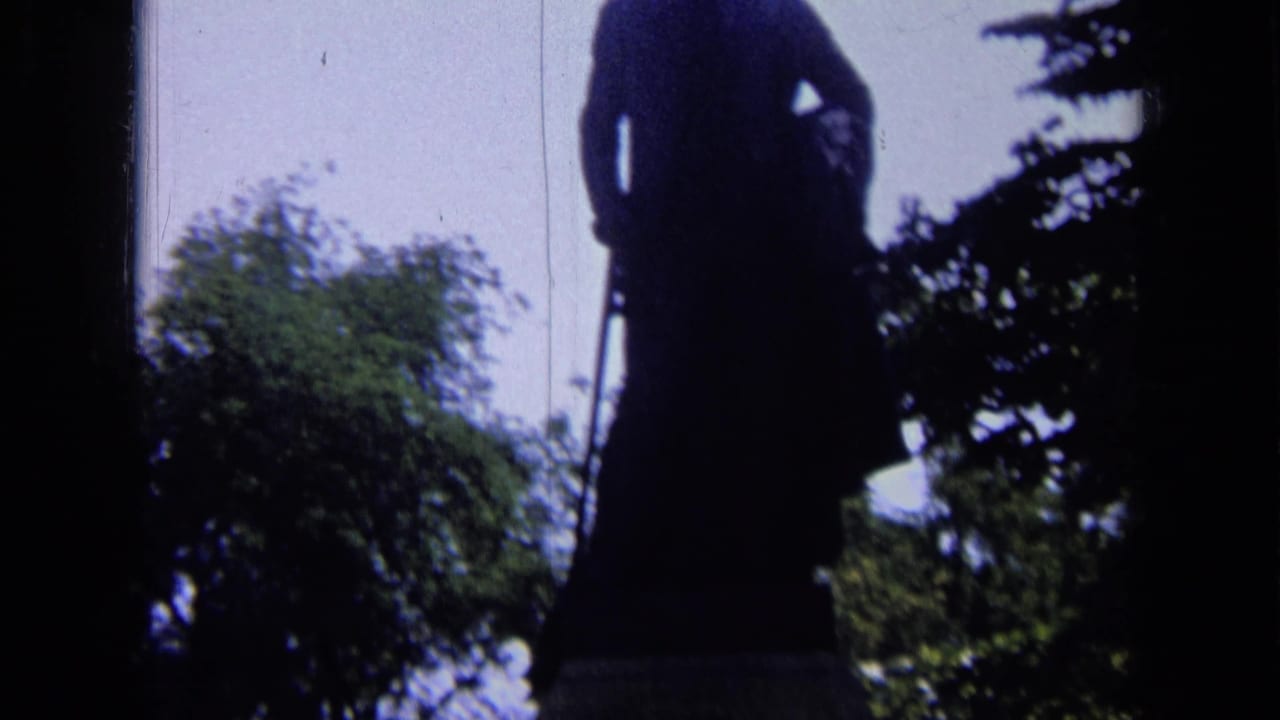 Dark silhouetted statue against bright sky with trees nearby.