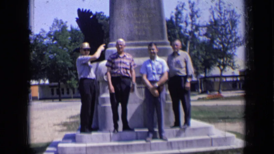 The group remains arranged on the monument steps in 1963 Russia footage, with trees and a low building visible behind them.