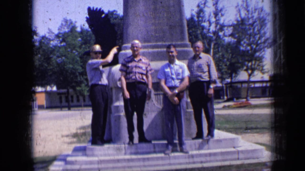 Four men standing near the base of a monument in bright daylight.