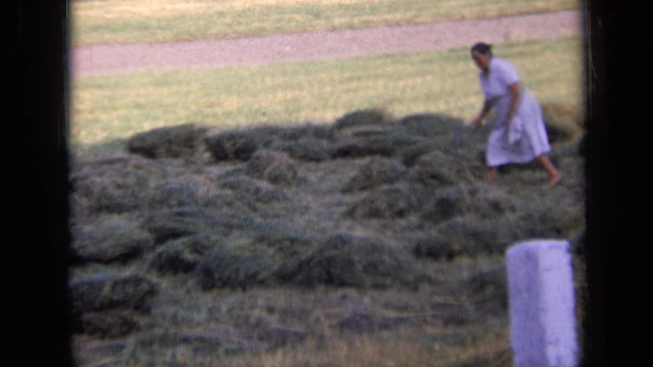Woman in a light dress walking among hay piles in a grassy field.