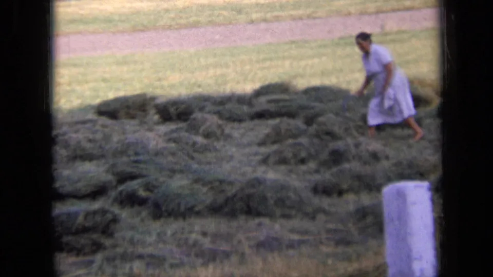 In 1963 Russia, a woman in a light dress moves through scattered hay piles in a rural field, framed by black 8mm borders.