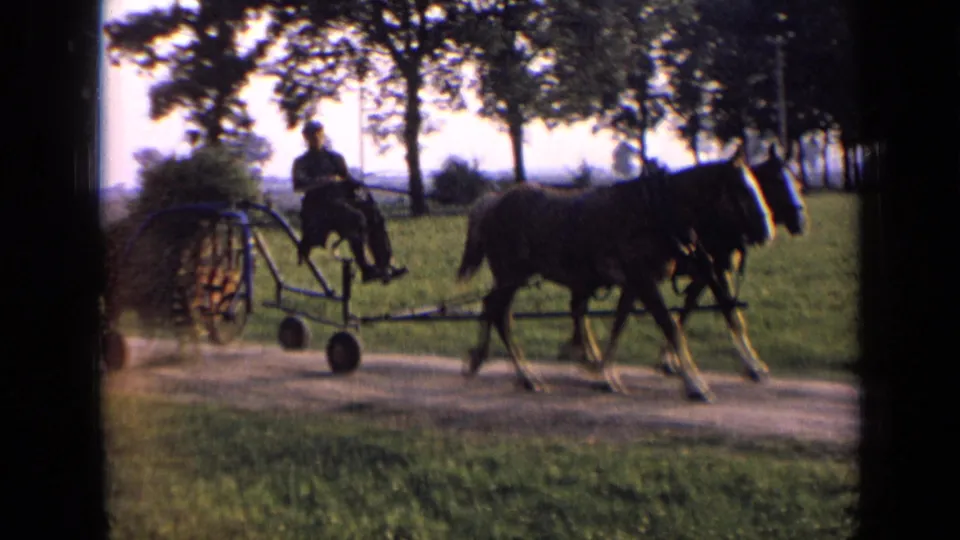 The horse-drawn implement passes nearer the camera, showing the horses, seated rider and wheeled frame on a rural Russia dirt road.