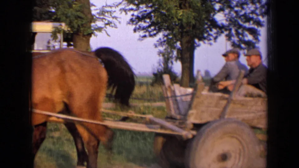The wagon passes the camera, showing the horse team, wooden cart bed, and several seated passengers in rural Russia.