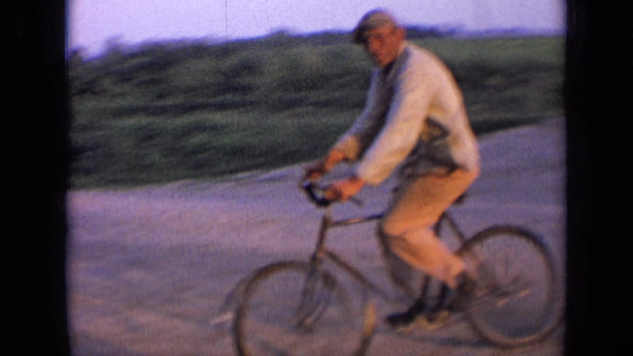 Man in a flat cap rides a bicycle along a rural dirt road.