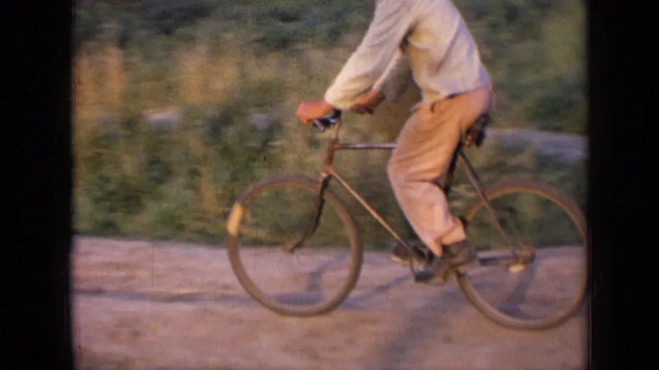 1963 Russia home-movie frame showing the man cycling across a rural road, with soft focus, grass, and handheld framing.