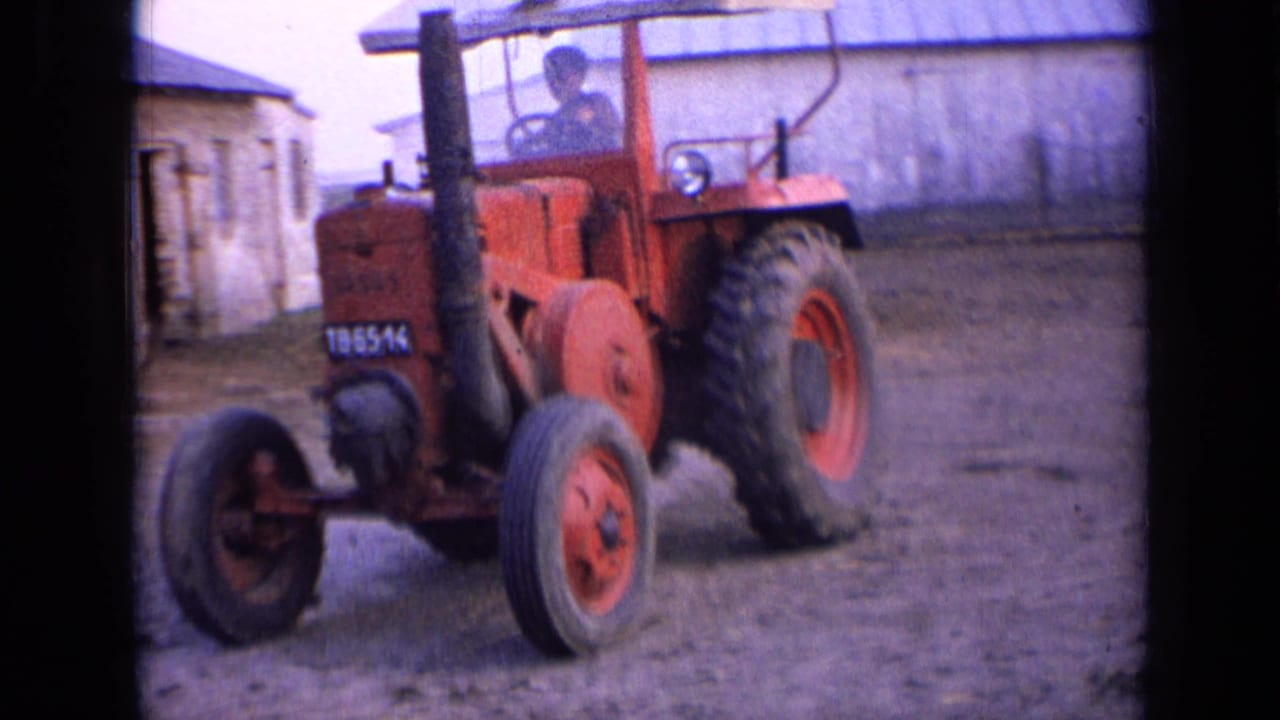 Red tractor in a Russian farmyard in 1963, with a driver in the cab and weathered masonry buildings behind it.
