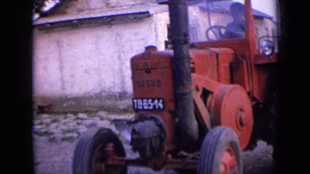 Closer view of the red tractor passing a plastered wall and stonework.