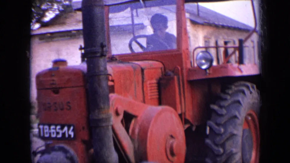 Close 1963 Russia home-movie view of the tractor cab and driver as the red machine moves through the yard.