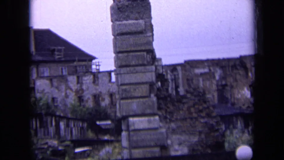 View across the farmyard toward a masonry pillar, stone wall, and weathered buildings in the same 1963 Russia home-movie clip.