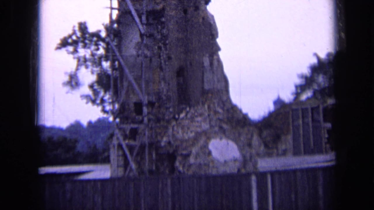 1963 Russia 8mm frame showing a weathered stone ruin with scaffolding, foliage, and a wooden fence viewed through a dark frame.