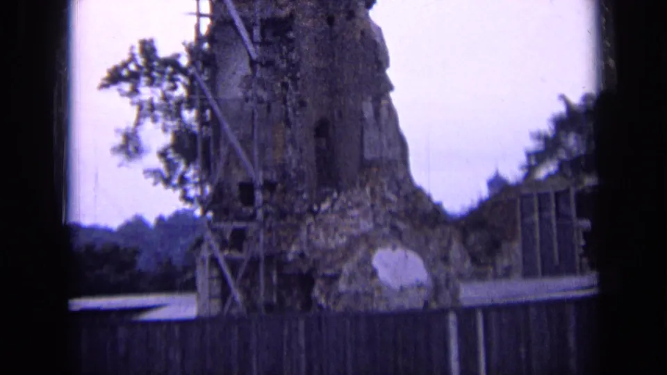 1963 Russia 8mm frame showing a weathered stone ruin with scaffolding, foliage, and a wooden fence viewed through a dark frame.