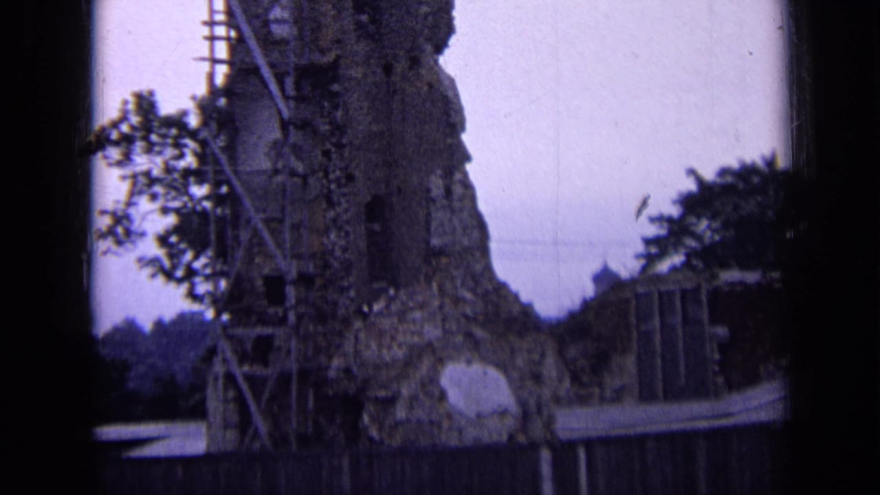 1963 Russia 8mm frame of a damaged masonry wall with scaffold poles, nearby foliage, and a wooden fence in the foreground.